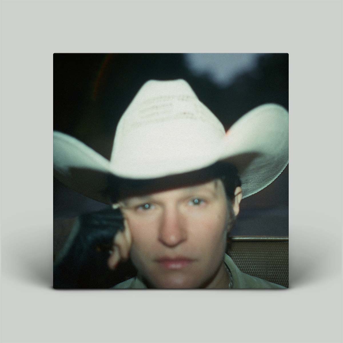 The image shows the album cover featuring a person with a contemplative expression, wearing a white cowboy hat.