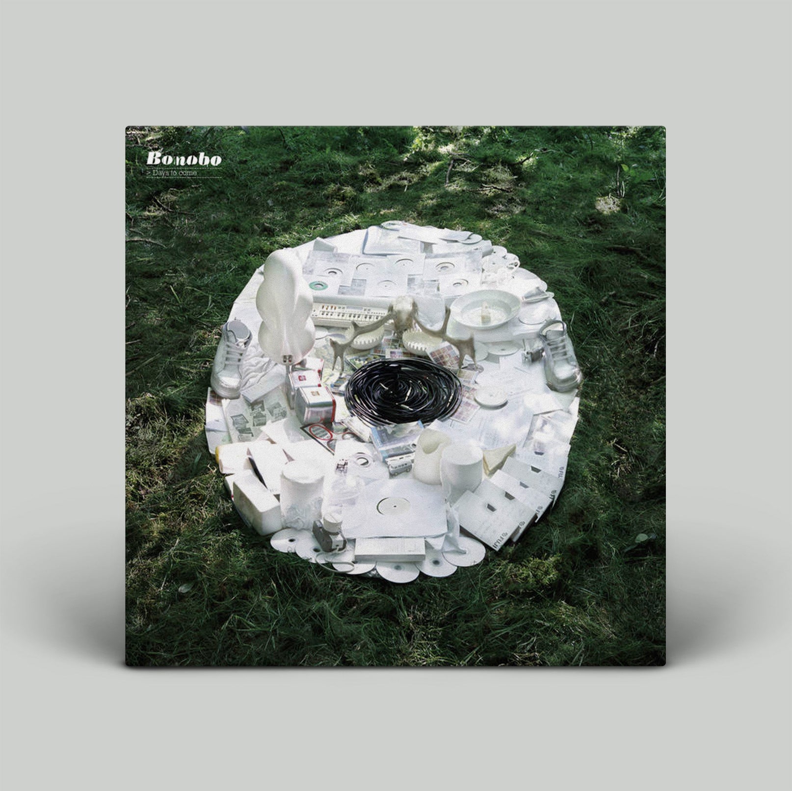 Vinyl record cover with a white abstract design on a grassy background, featuring the brand 'Bonobo'.