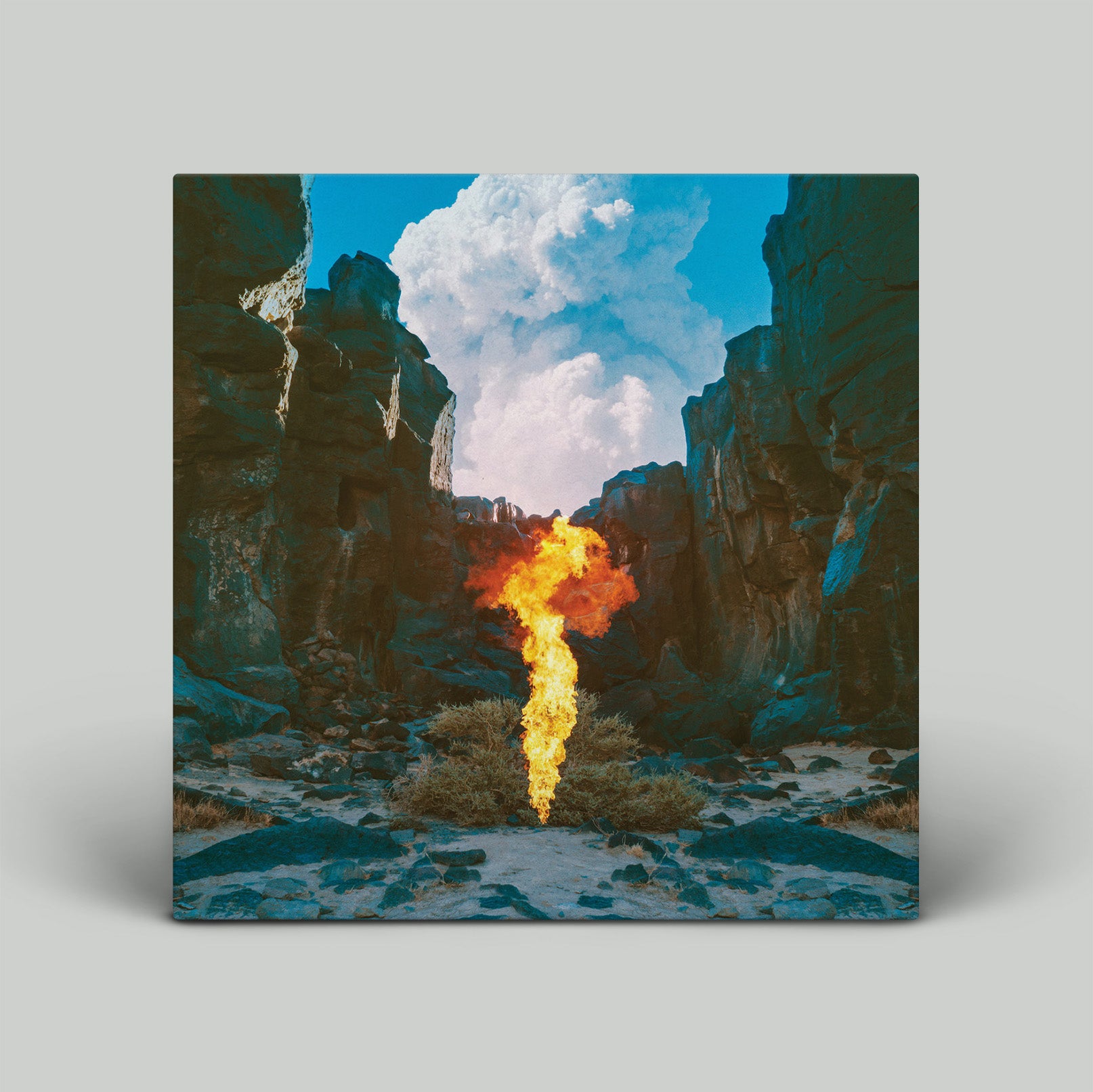 Flame in a desert landscape with rocky cliffs and a blue sky.