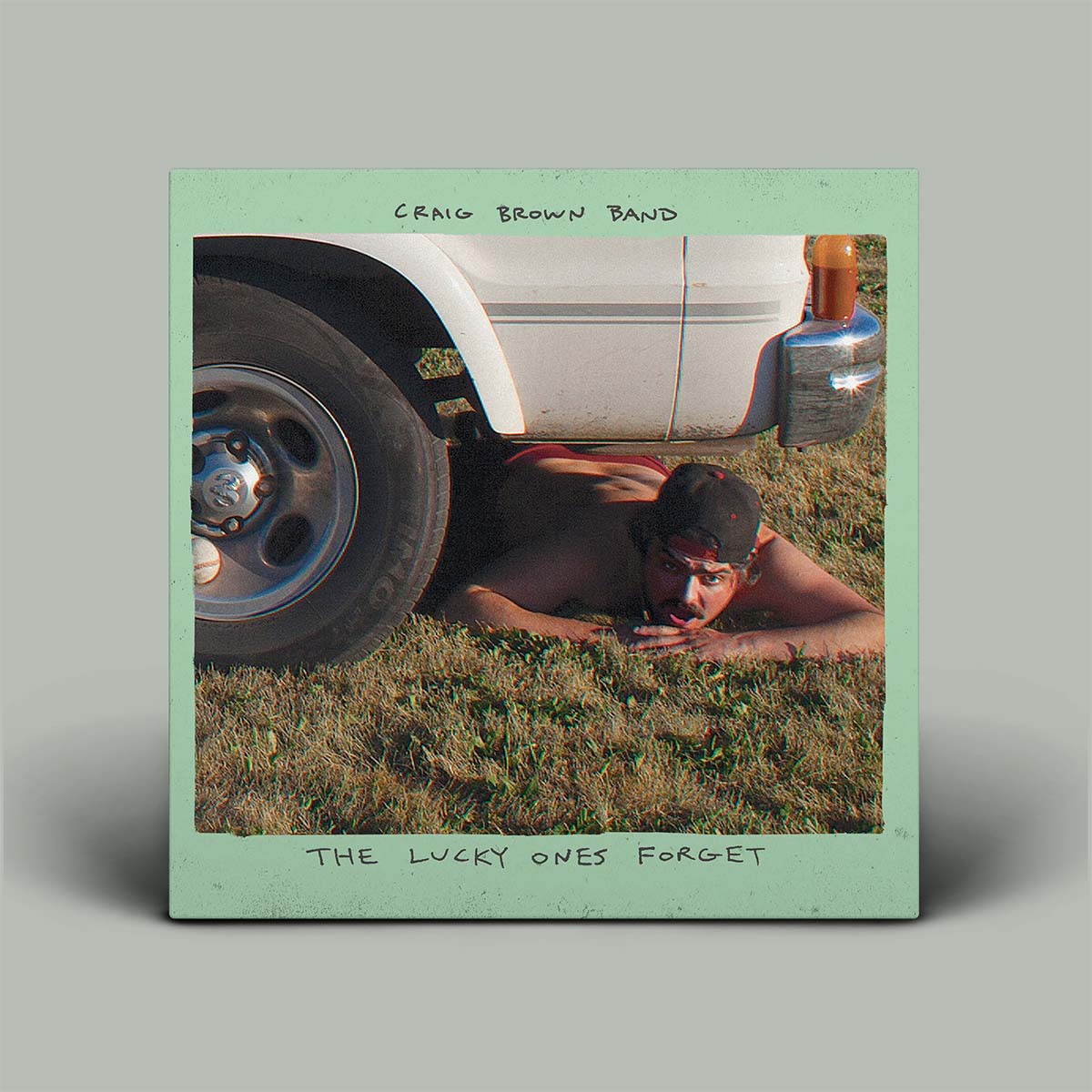 Album cover with a person lying on grass next to a car, featuring text 'Craig Brown Band' and 'The Lucky Ones Forget'.