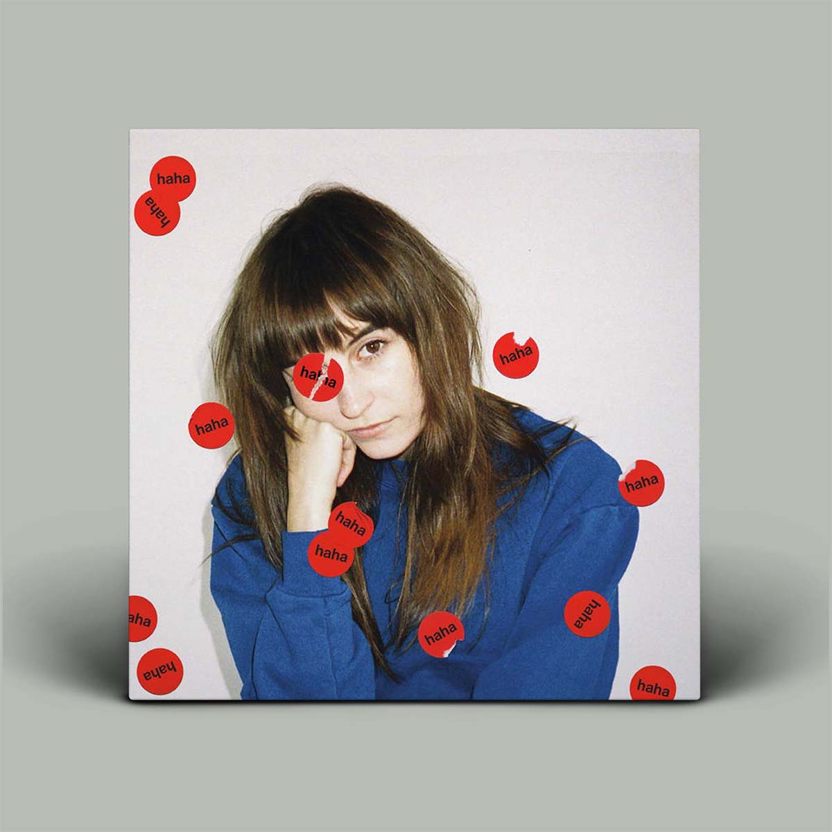 Album cover with a person wearing a blue jacket surrounded by red stickers with 'haha' text on a gray background