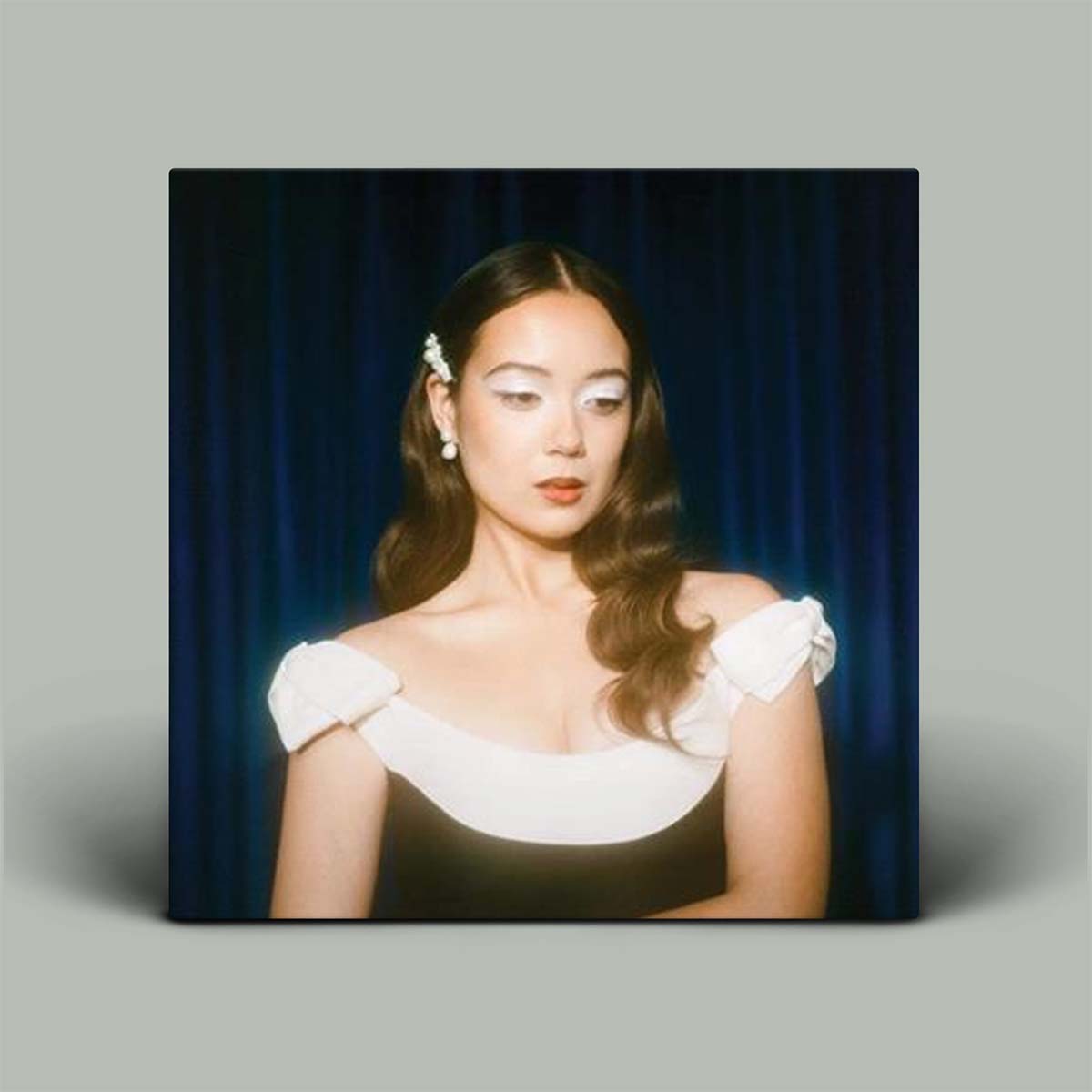 Woman wearing a white dress with puffed sleeves against a dark blue curtain.