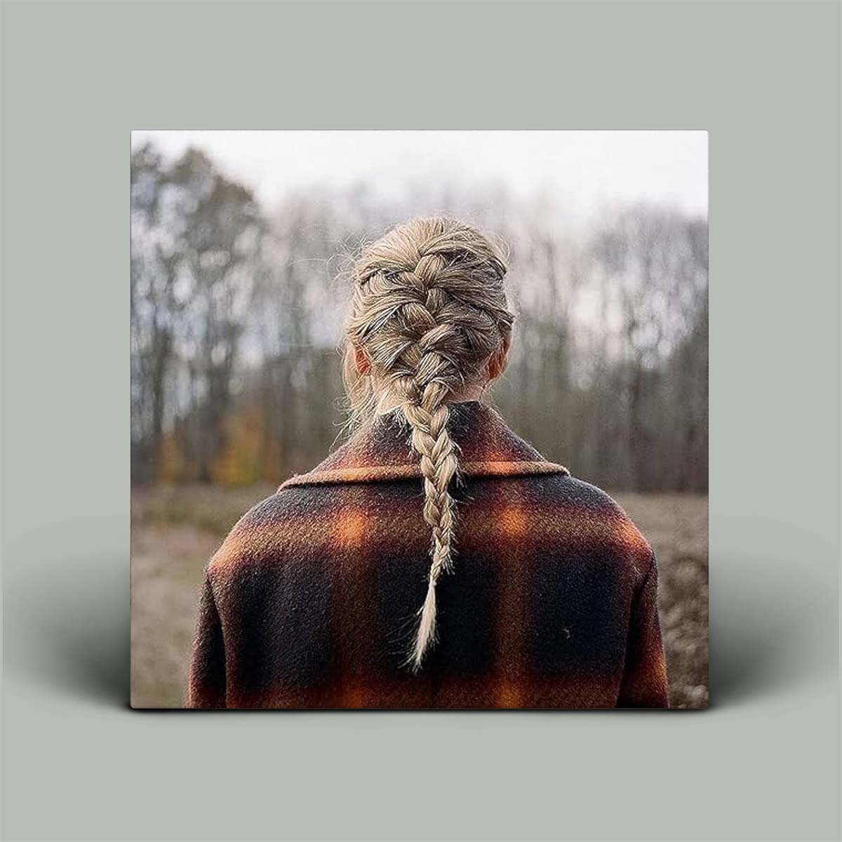 Album cover with person with braided hair wearing a plaid coat in a forest setting