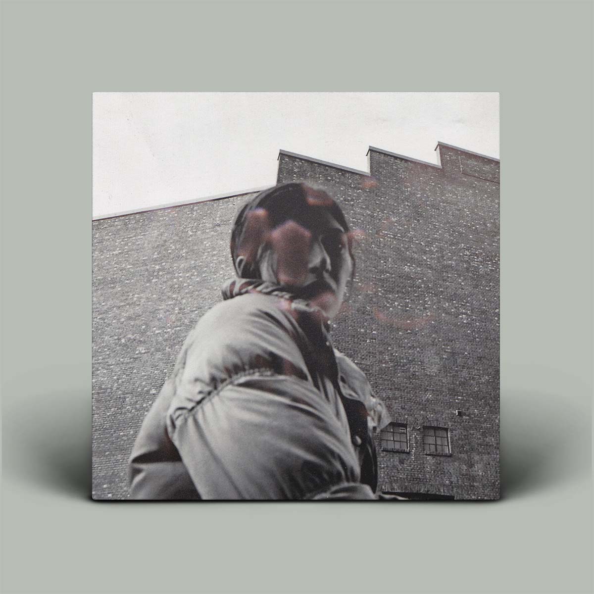 Person wearing a coat with a blurred face against a brick wall