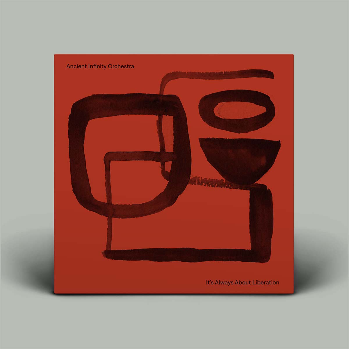 A square album cover for the Ancient Infinity Orchestra's 'It's Always About Liberation' stands against a neutral gray background. The cover features a bold terracotta red background with dark brown abstract watercolor-like shapes and black text.