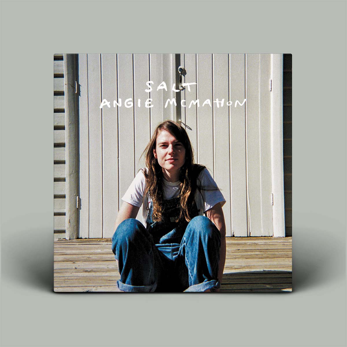 Album cover with a person sitting on a wooden bench against a white paneled wall, featuring the text 'Salt' and 'Angie McMahon'.