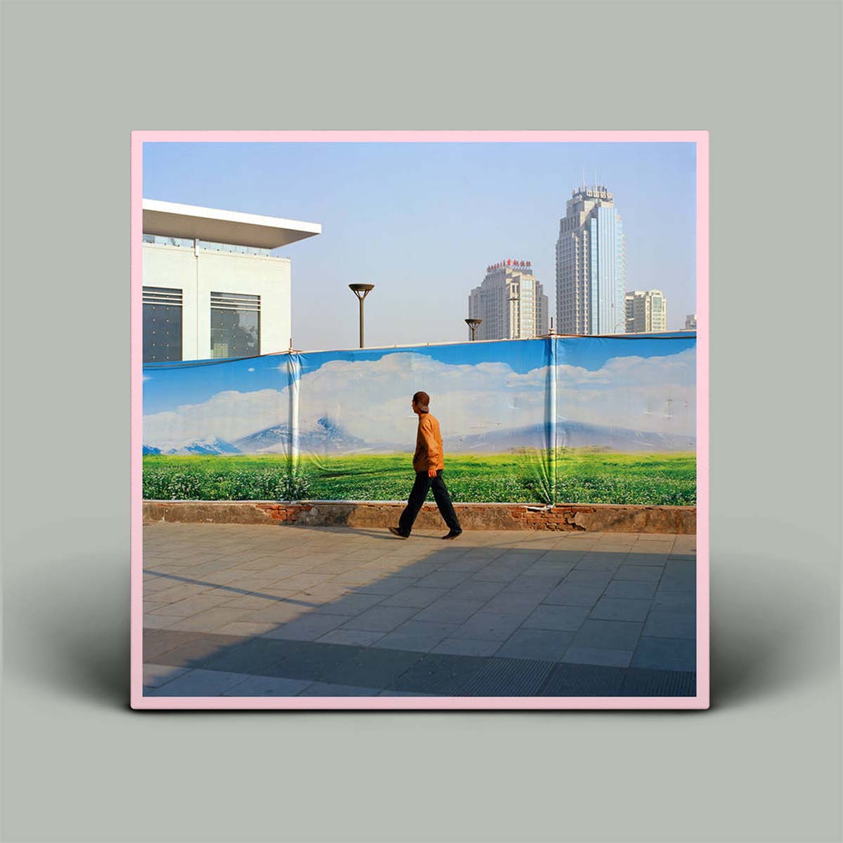 Album cover featuring a scenic landscape with a person walking in front of a green field and modern buildings, displayed on a light gray background with a drop shadow.