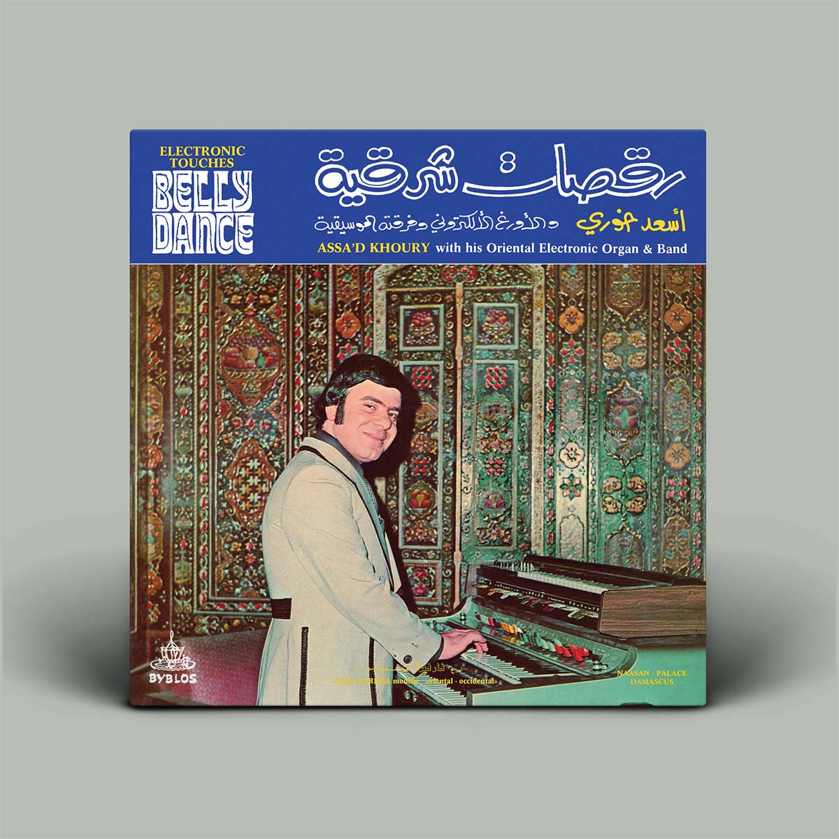 A vinyl record album cover for 'Belly Dance' by Assad Khoury, featuring a blue header with white and gold text and an illustration of a man playing an oriental organ in front of patterned rugs. The record is shown on a neutral gray background.