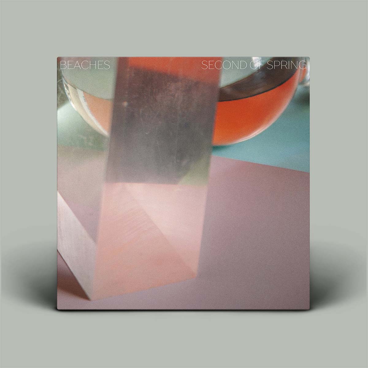 A square album cover for 'Beaches - Second Of Spring' displayed against a solid gray background. The cover art features an abstract photograph with a translucent pink block, a glass of pink beverage, and a soft pink surface.