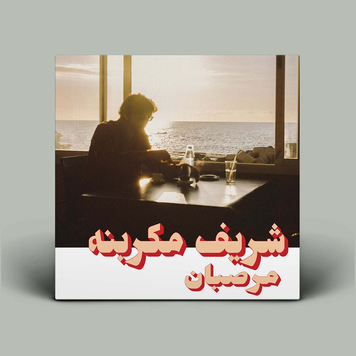 Album cover with a silhouette of a person at a table by the sea, with Arabic text on a gray background.
