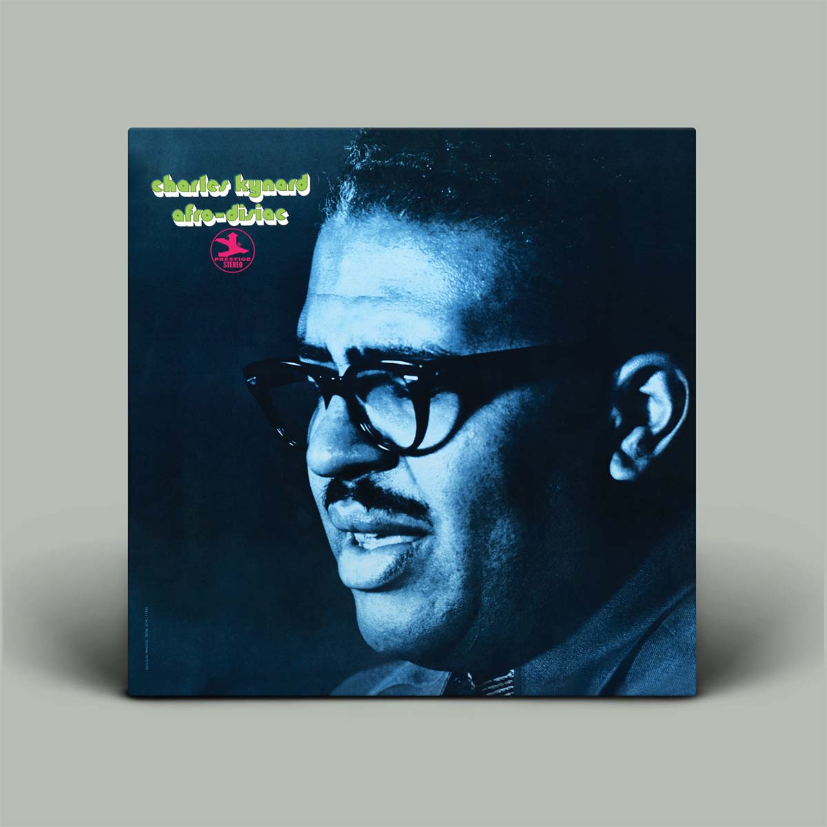 A vinyl record album cover stands upright against a neutral gray background. The cover features a dramatic blue-toned portrait of the jazz musician wearing glasses, with yellow-green text and a small red logo in the top left corner.