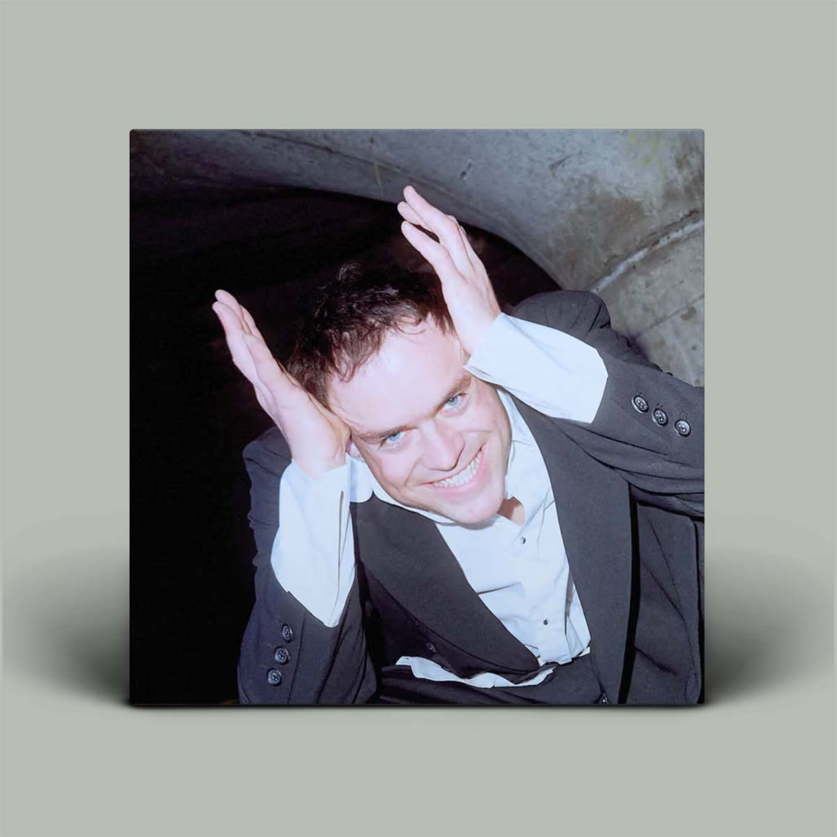 Person in formal attire with hands on head against a neutral background