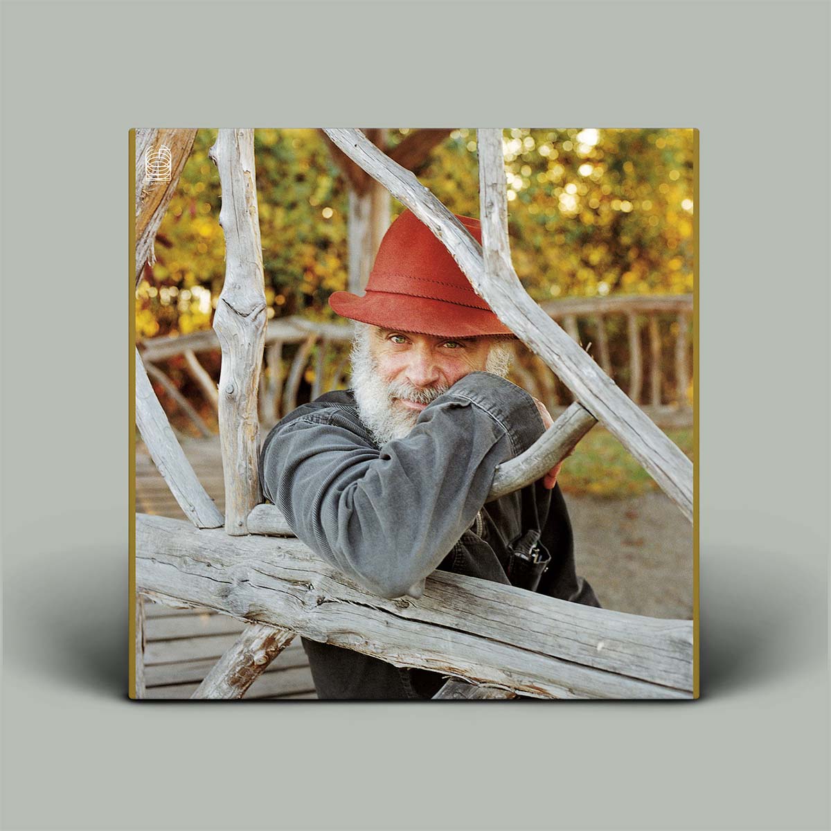 Man with a red hat and gray jacket leaning against wooden beams with a blurred natural background