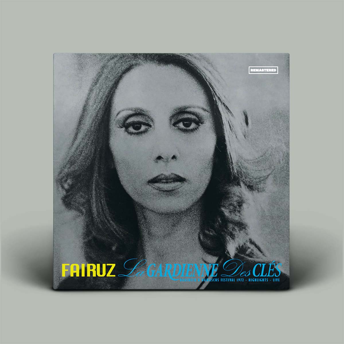 A square album cover for Fairuz's 'La Gardienne Des Clés' stands upright against a light gray background. The cover features a black-and-white portrait of the artist, with the title in blue script and 'FAIRUZ' in yellow at the bottom left.
