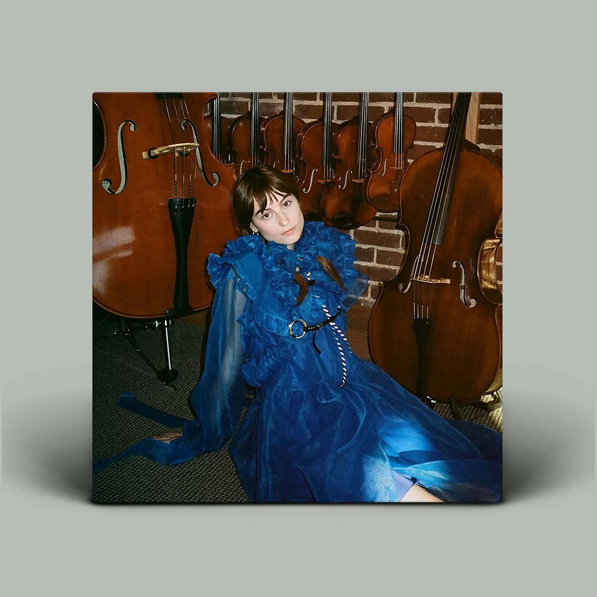 Woman in a blue dress sitting among stringed instruments with a brick wall background