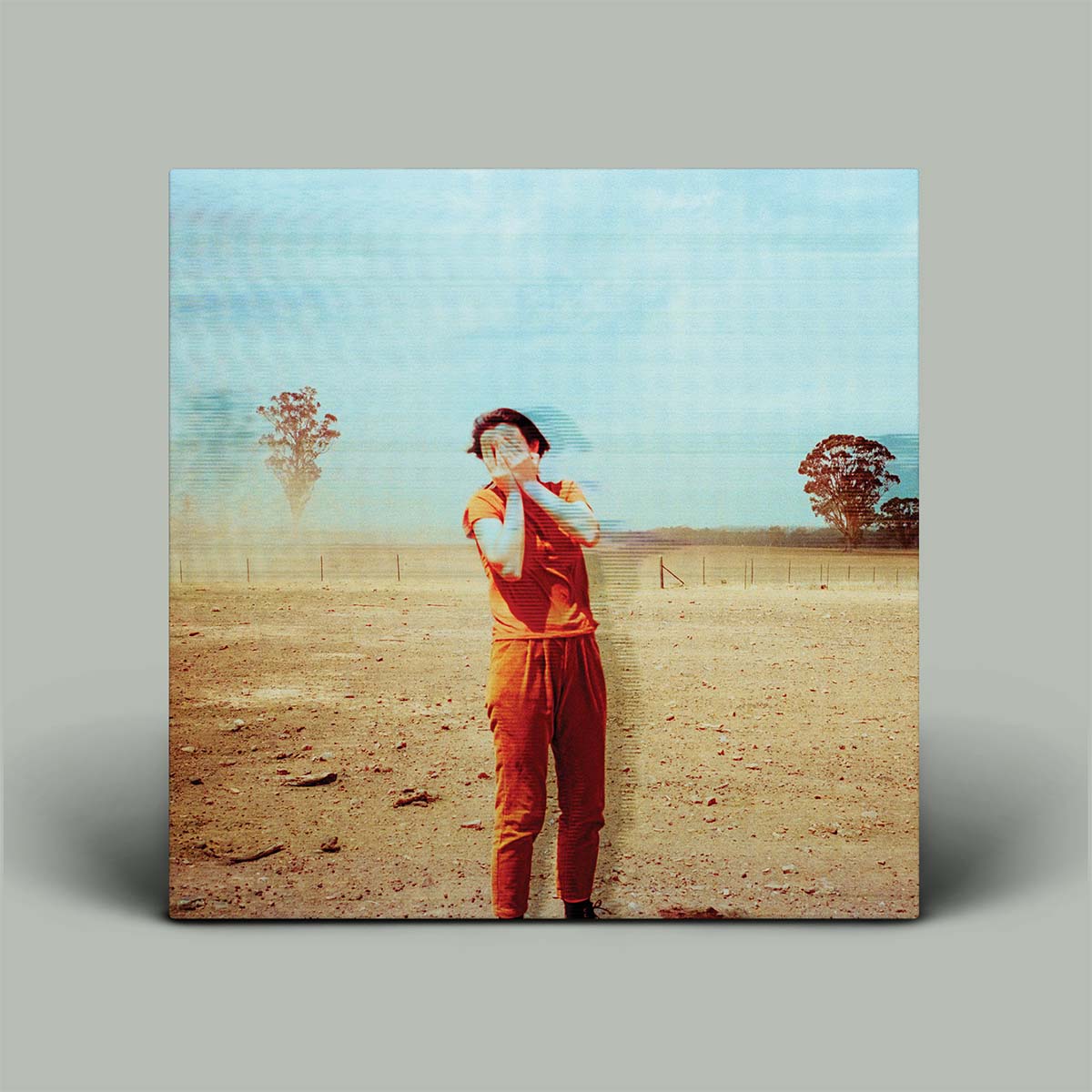 Person in orange jumpsuit standing in a field with a blue sky and trees.