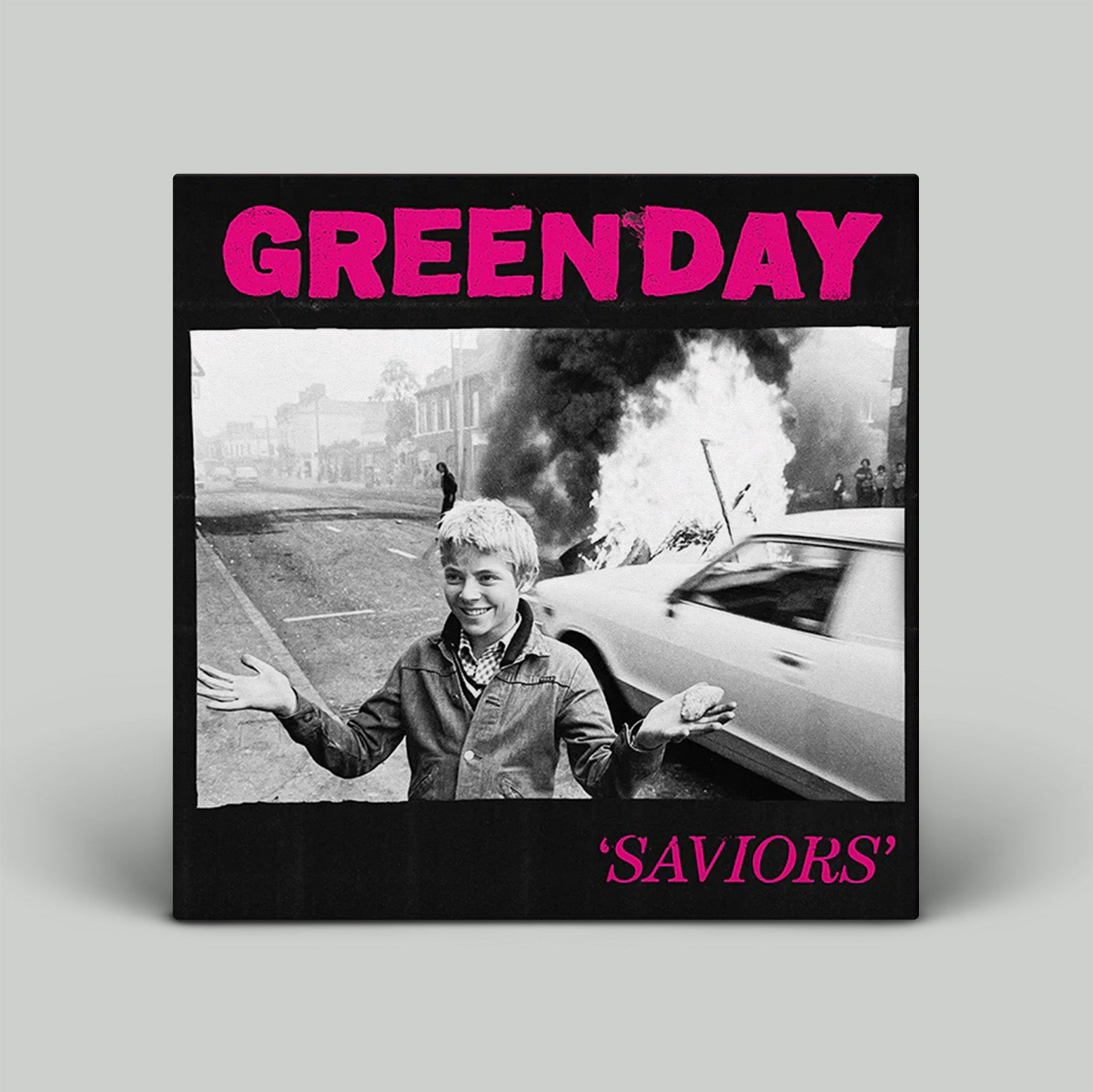 Album cover for Green Day's 'Saviors' with a black and white photo of a boy and pink text on a gray background