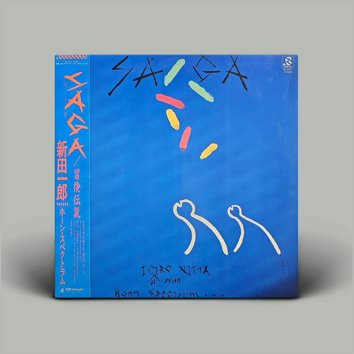 A square vinyl record sleeve for 'SAGA' featuring a bright blue background with abstract hand-drawn white line art, colorful paint strokes, and orange/red Japanese text on the spine, photographed on a neutral gray background.