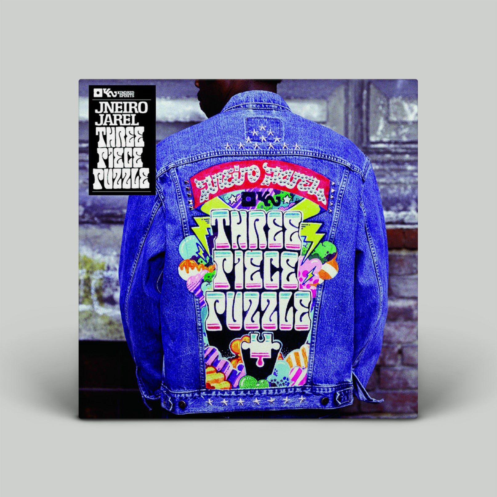 Denim jacket with colorful 'Three Piece Puzzle' design on a gray background