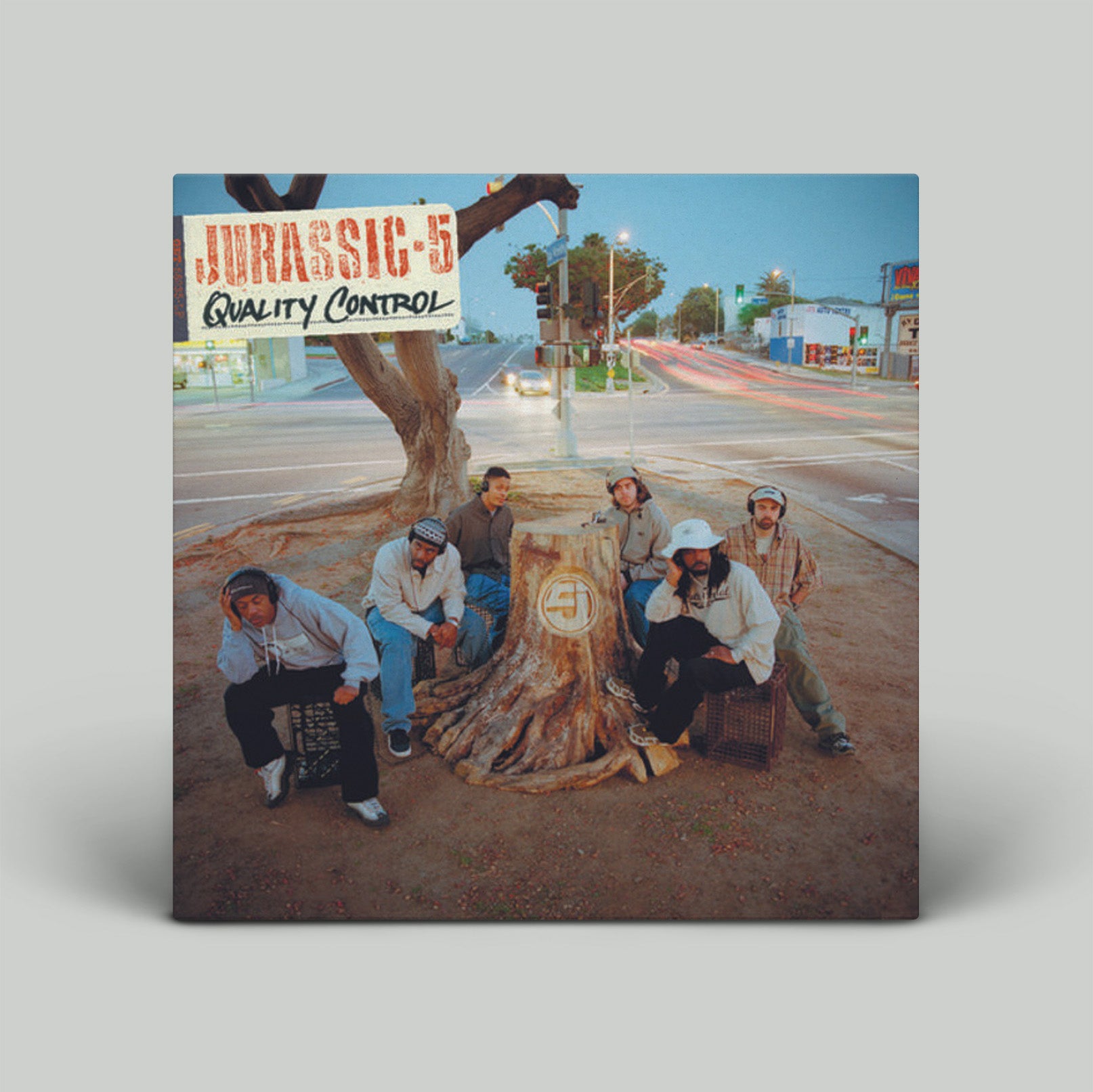 Album cover with a group of people around a tree stump on a street, with 'Jurassic 5 Quality Control' text.