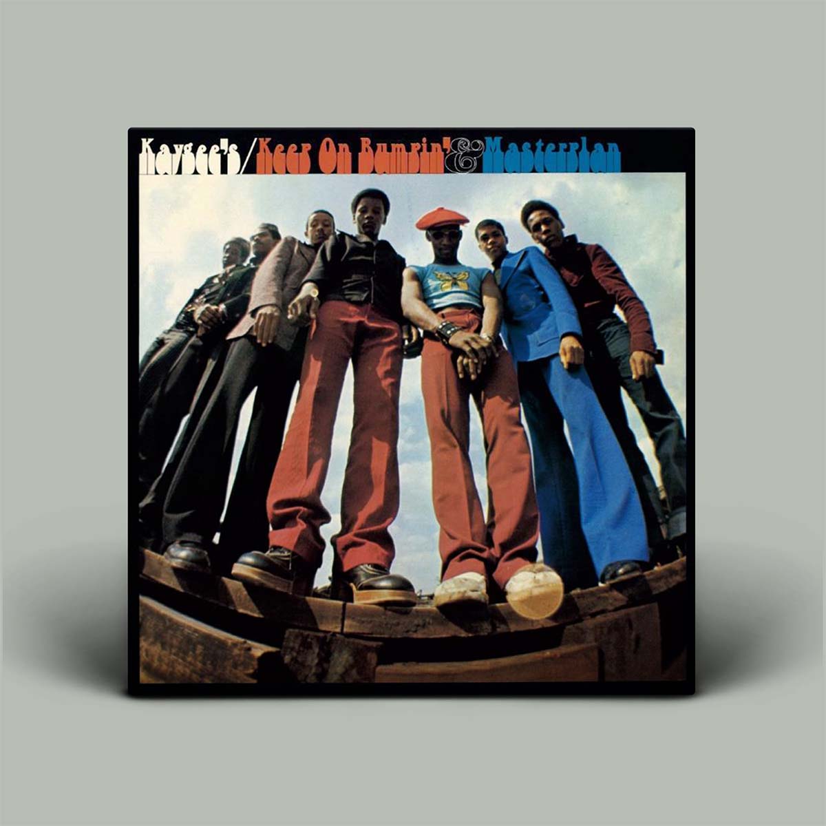 The album cover for Kaygee's 'Keep On Bumpin' & Masterplan' is shown as a square product mockup against a solid gray background. The cover art features a group of seven young men standing on a wooden structure against a cloudy sky, with the album title in stylized multicolor text at the top.