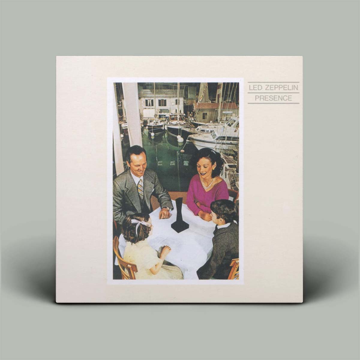 Led Zeppelin 'Presence' vinyl record sleeve shown standing upright against a plain gray background. The cover has a wide cream border around a central vintage-style photograph of people seated by a waterfront with boats.