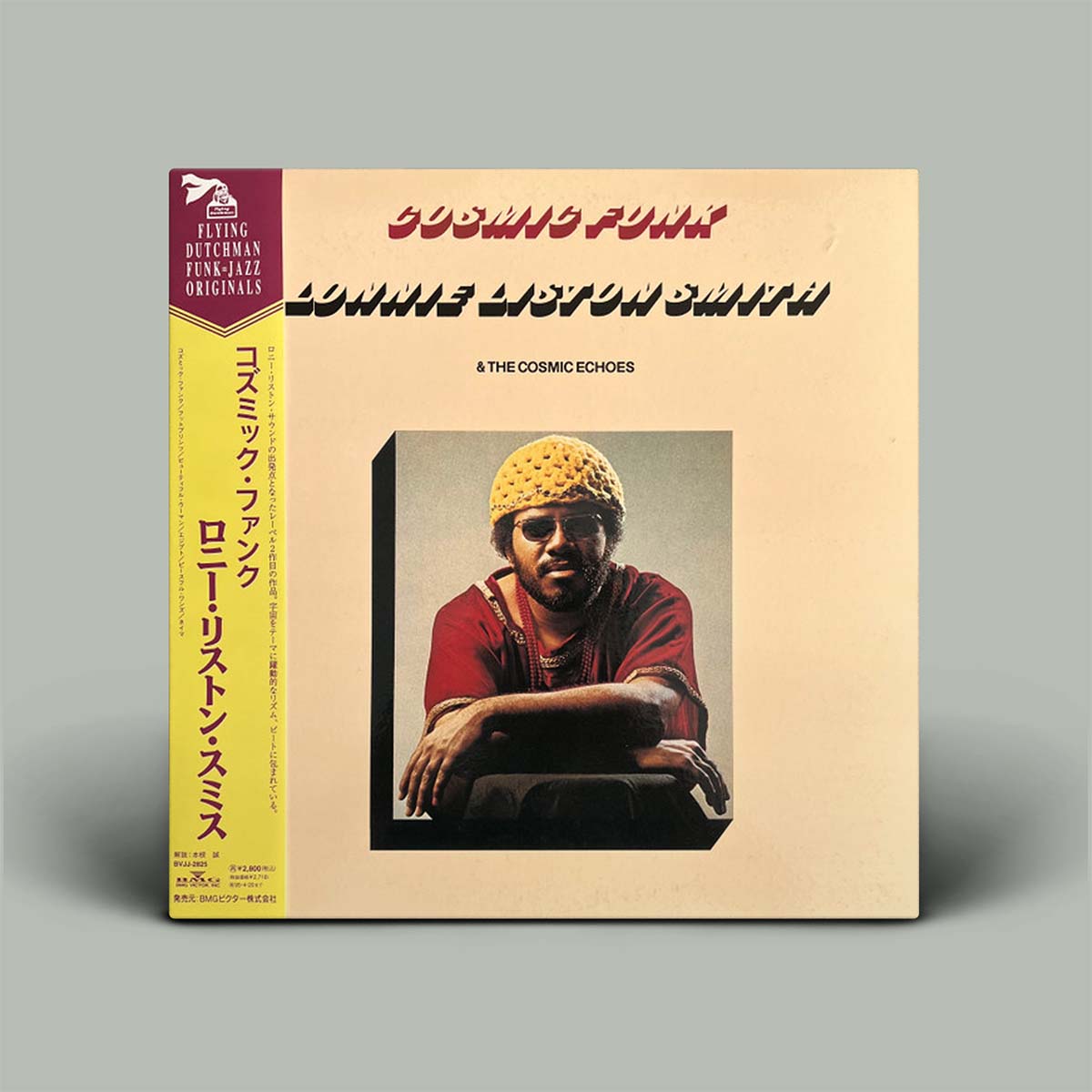 Vinyl record cover with a person wearing a yellow hat and red shirt, featuring text and a logo on a beige background.