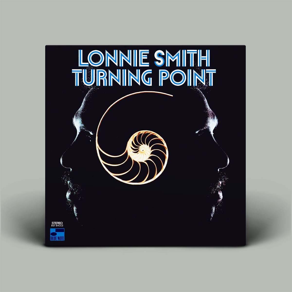 Lonnie Smith 'Turning Point' vinyl record cover, featuring a black background with a gold spiral shell graphic and the artist's name in blue text, shown standing against a neutral gray background.