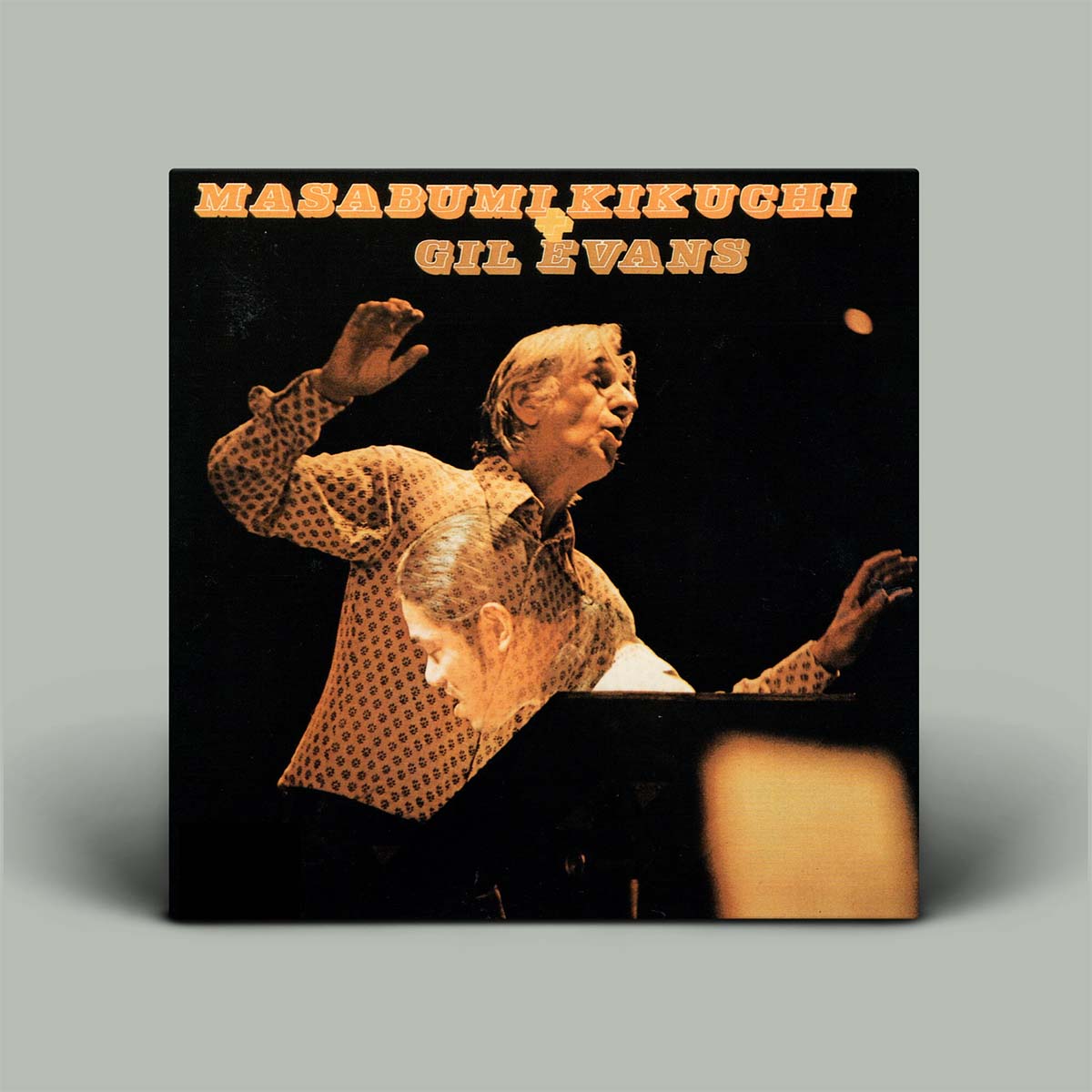A square album cover for MasaBumi Kikuchi and Gil Evans stands against a plain light gray background. The cover art shows a warm-toned photograph of a musician at a piano against a dark background, with the text 'MASABUMI KIKUCHI' and 'GIL EVANS' in orange at the top.