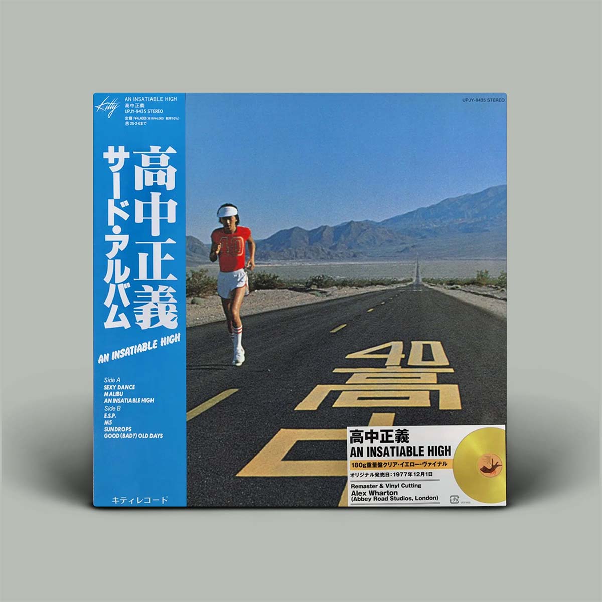 Japanese vinyl record cover for 'An Insatiable High', featuring a blue spine with white text, a desert road scene with a runner, and a gold disc graphic on the front, shown against a neutral gray background.