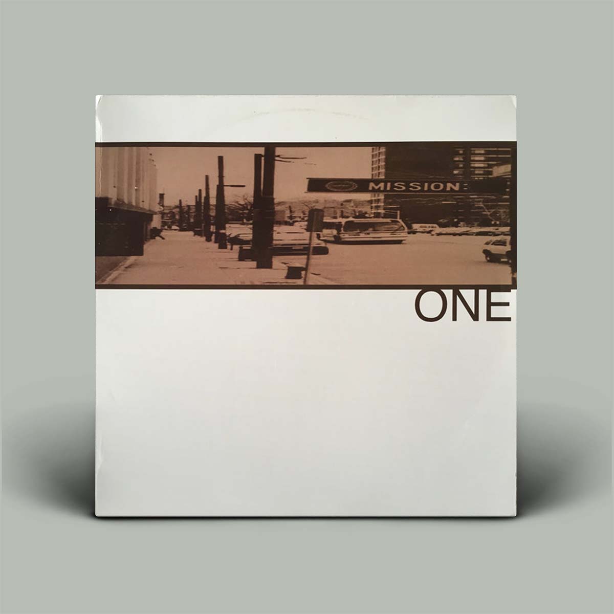 A square album or book-style cover standing upright on a light gray background. The cover is mostly off-white with a horizontal sepia-toned street photograph across the upper middle and the partial word 'ONE' printed in large black letters on the right side.