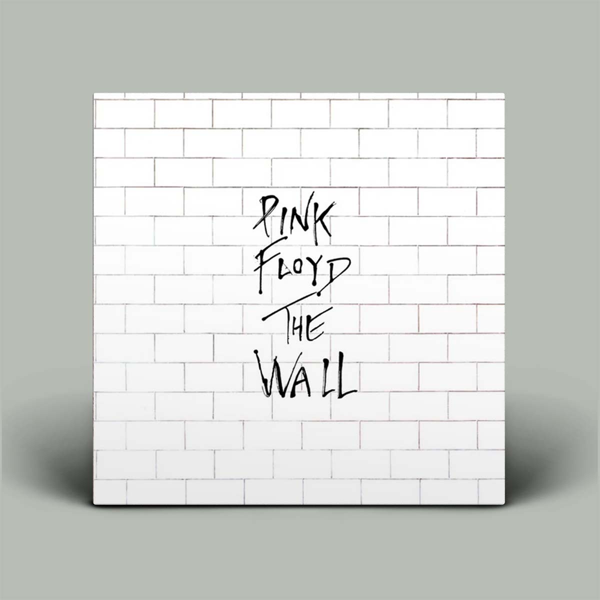 A square wall art print or canvas featuring a white subway-tile pattern with the text 'PINK FLOYD THE WALL' in black handwritten lettering, shown against a light gray background.