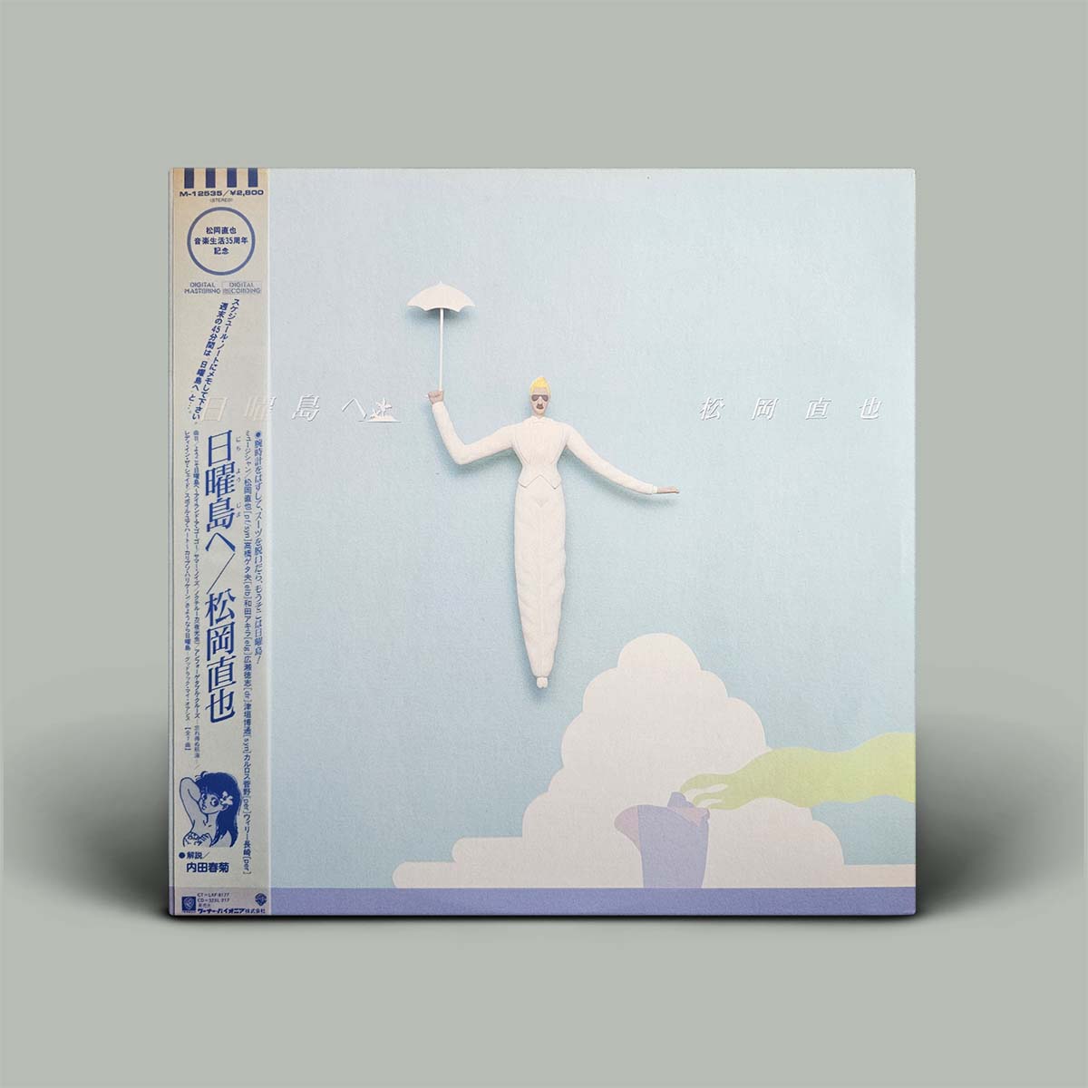 A square album or book-style package standing upright on a plain gray background. The front has a pale blue background with a stylized white figure holding a small umbrella above soft white cloud shapes, and a narrow printed spine strip on the left with blue text and graphics.