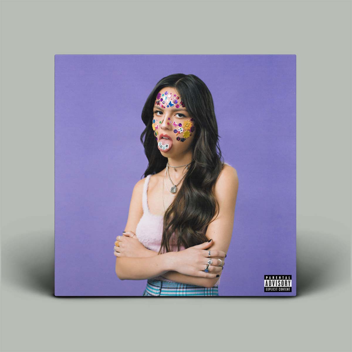 A album cover featuring a person with long hair, standing against a purple background, with a playful facial expression and colorful dot makeup on the face.