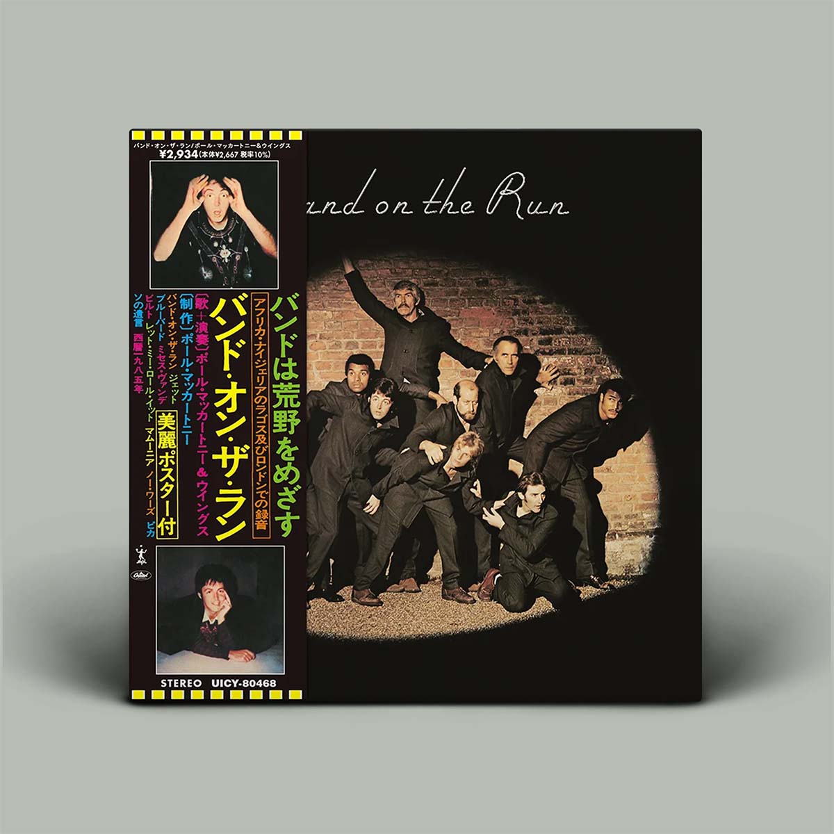The cover features a black background with a circular spotlight effect highlighting a group of men in dark clothing against a brick wall, with Japanese text and two portrait photos of the band members on the spine.