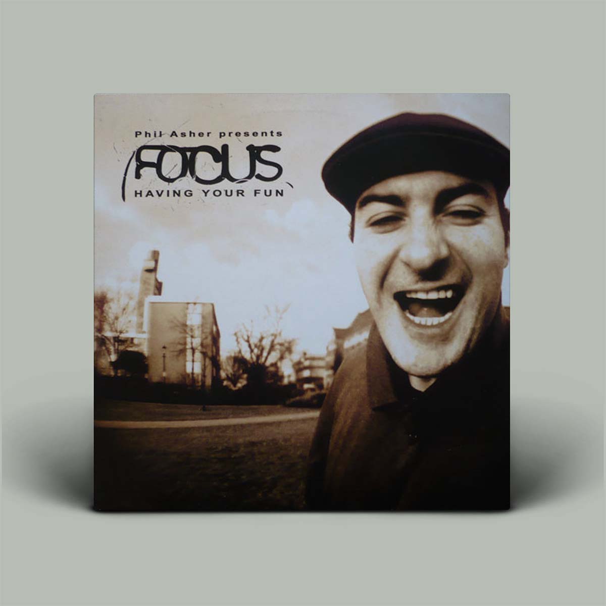 Album cover standing upright on a light gray background. The cover features a sepia-toned photograph of a smiling man wearing a dark cap, with the text 'Phil Asher presents Focus Having Your Fun' across the top.