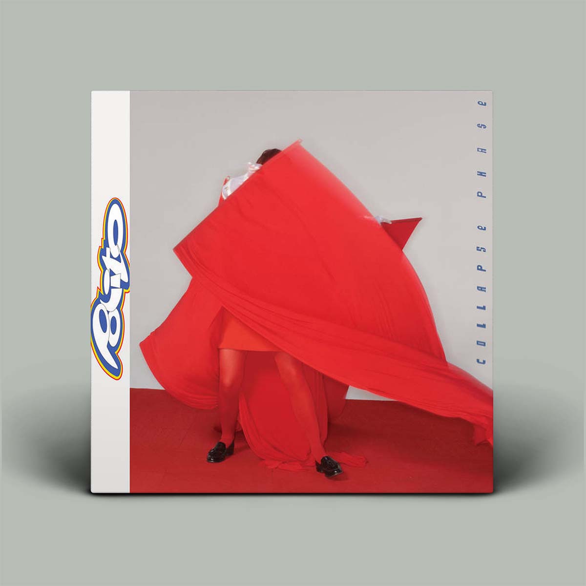 Person in a red dress with a large red fabric, standing against a gray background with a visible brand logo.