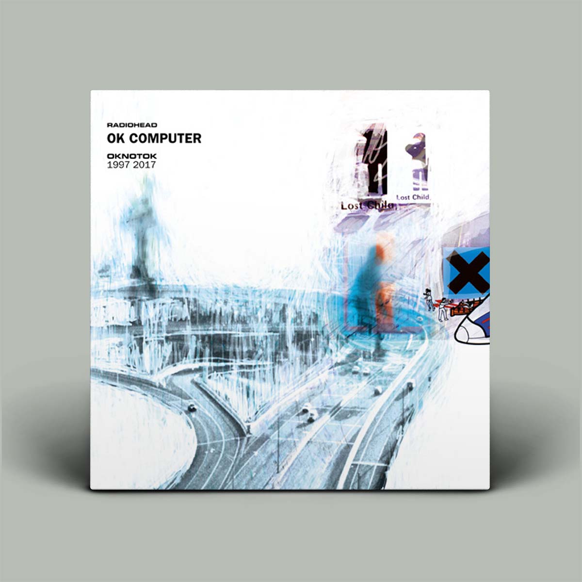 Radiohead's 'OK Computer' 12-inch vinyl record cover, featuring a white background with a blue-toned abstract cityscape graphic and tracklist details, shown on a neutral gray background.