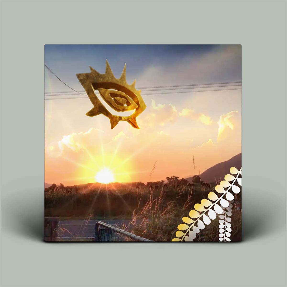Album with a sunset over a field, a golden symbol, and a leaf design on a gray background.