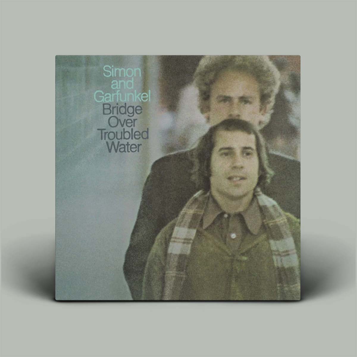 Album cover of 'Bridge Over Troubled Water' by Simon and Garfunkel with two individuals on a gray background.