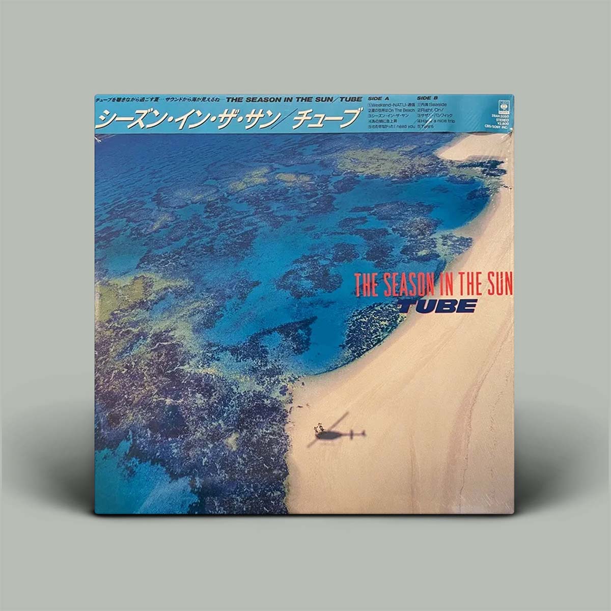 A vinyl record album cover for 'The Season in the Sun, Volume 2' by Tube, featuring an aerial photograph of a tropical beach and turquoise ocean. The cover is displayed against a solid gray background.