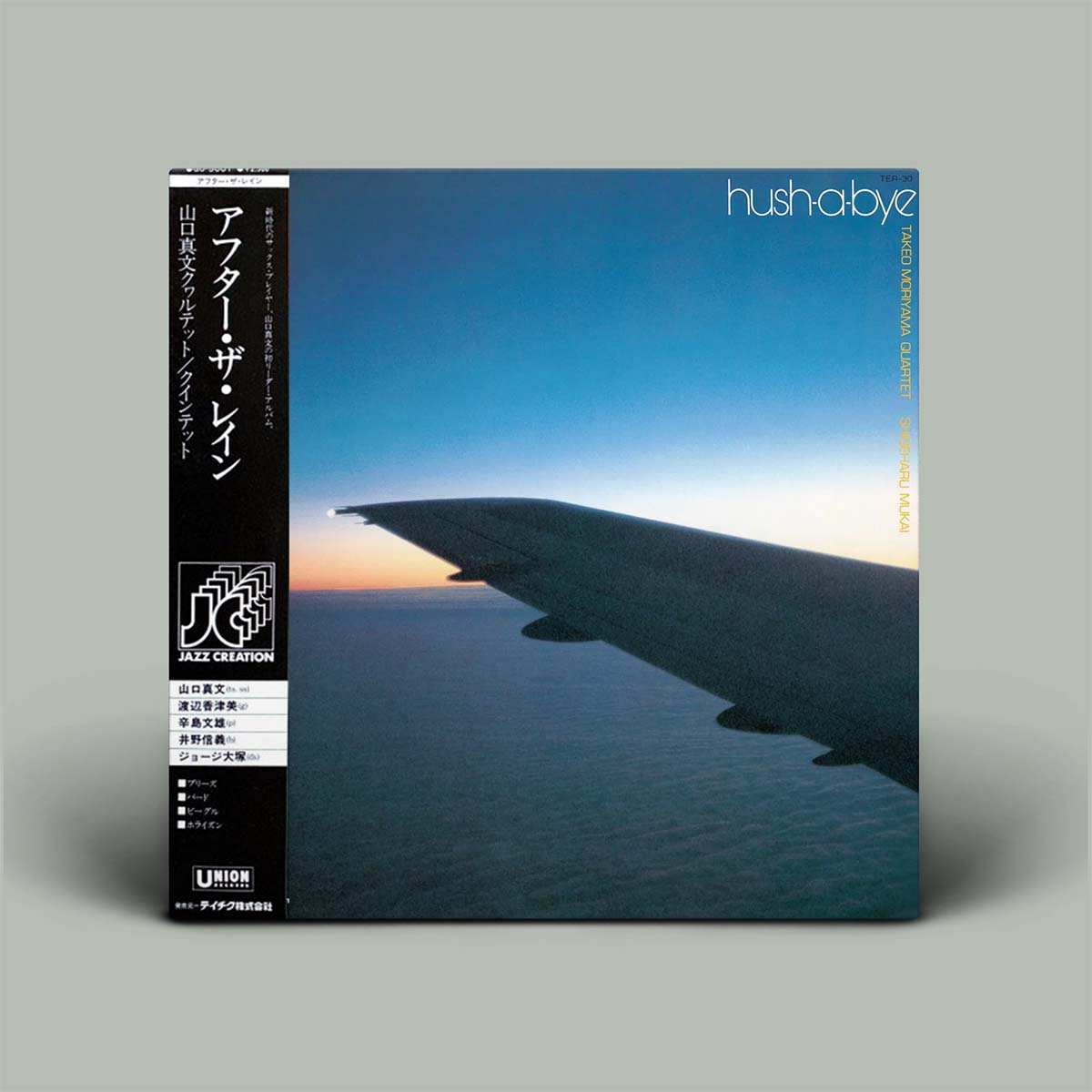 A square music album cover standing upright on a plain light gray background. The cover shows an airplane wing over water at dusk, with a black vertical spine band on the left and the word 'hushabye' printed near the top right.