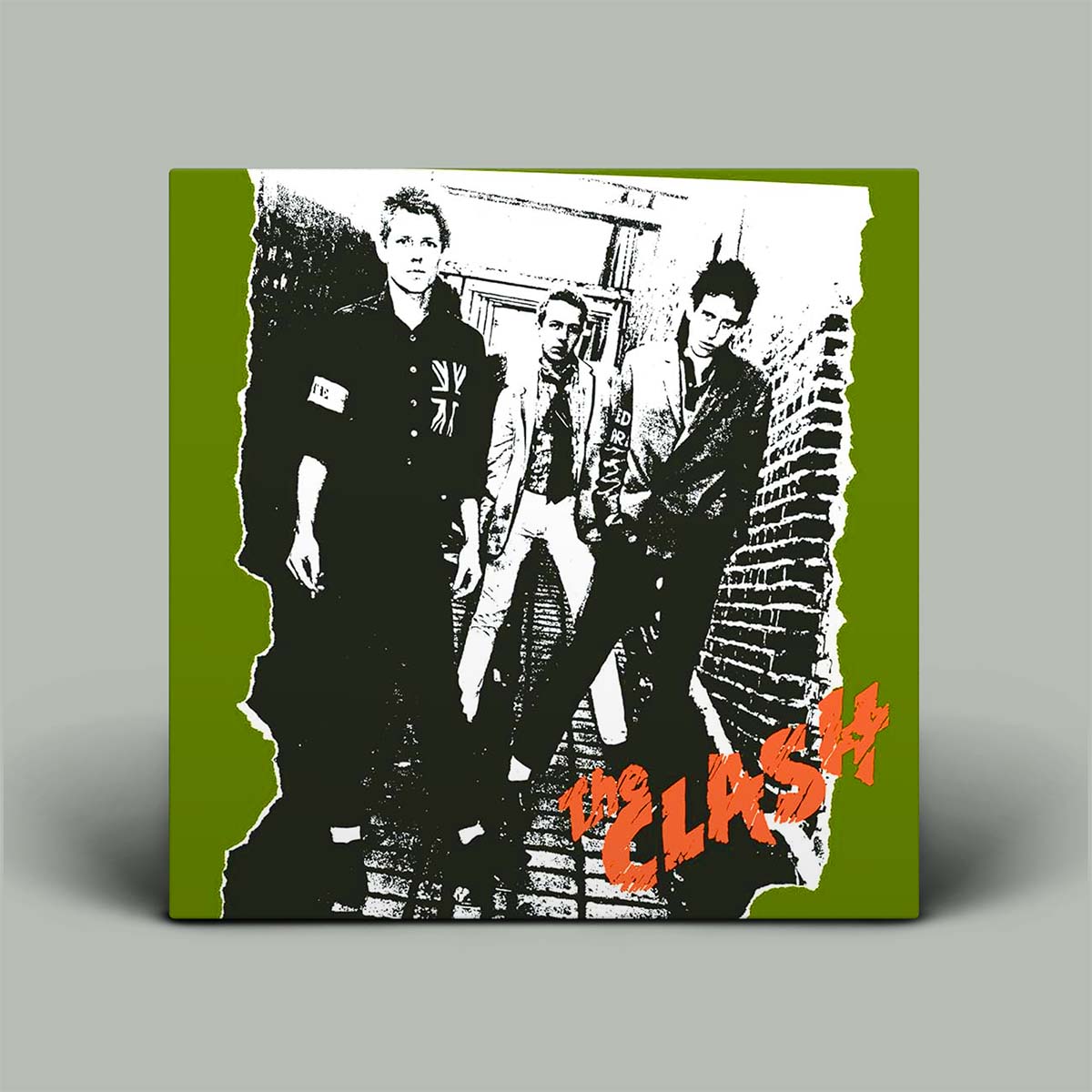 A square album cover for the band 'The Clash' displayed against a neutral gray background. The cover features a black and white graphic photo of the band members with a torn-paper effect, set on an olive green background with the band's name in orange text.