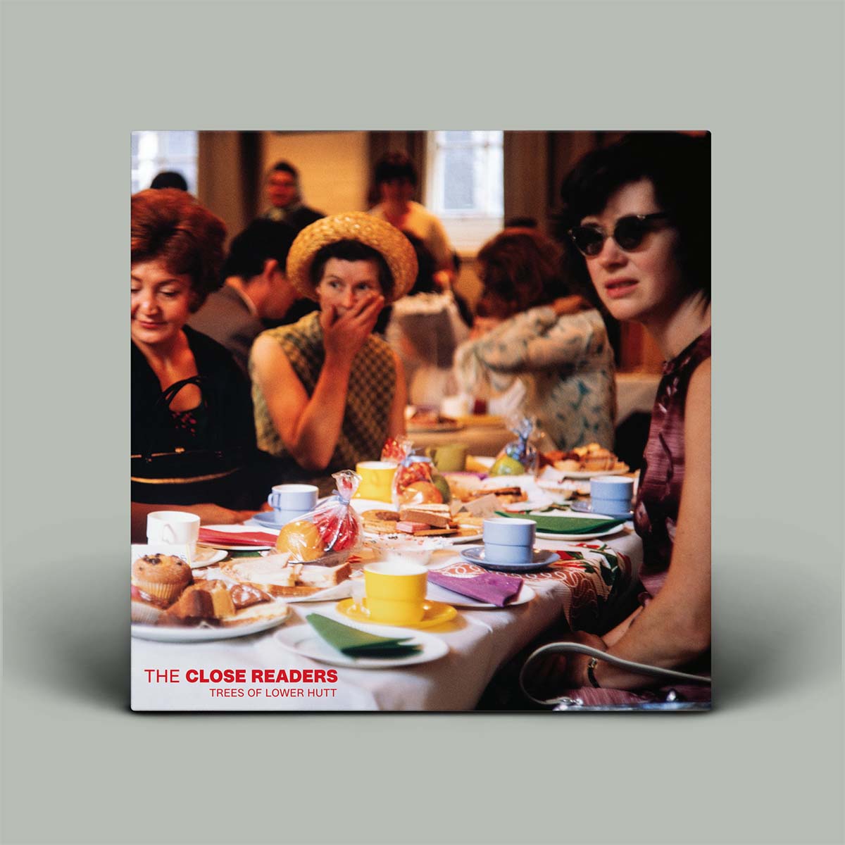 A square album cover featuring a vintage cafe scene with people seated at a table, photographed against a plain light gray background. The cover text at the bottom reads 'THE CLOSE READERS' and 'TREES OF LOWER HUTT'.