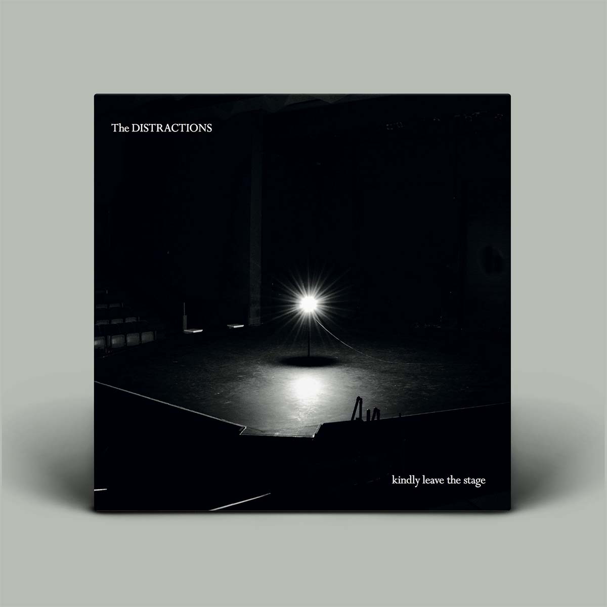 The Distractions 'kindly leave the stage' vinyl record cover, featuring a dark, moody photograph of a stage with a spotlight on a gray background.