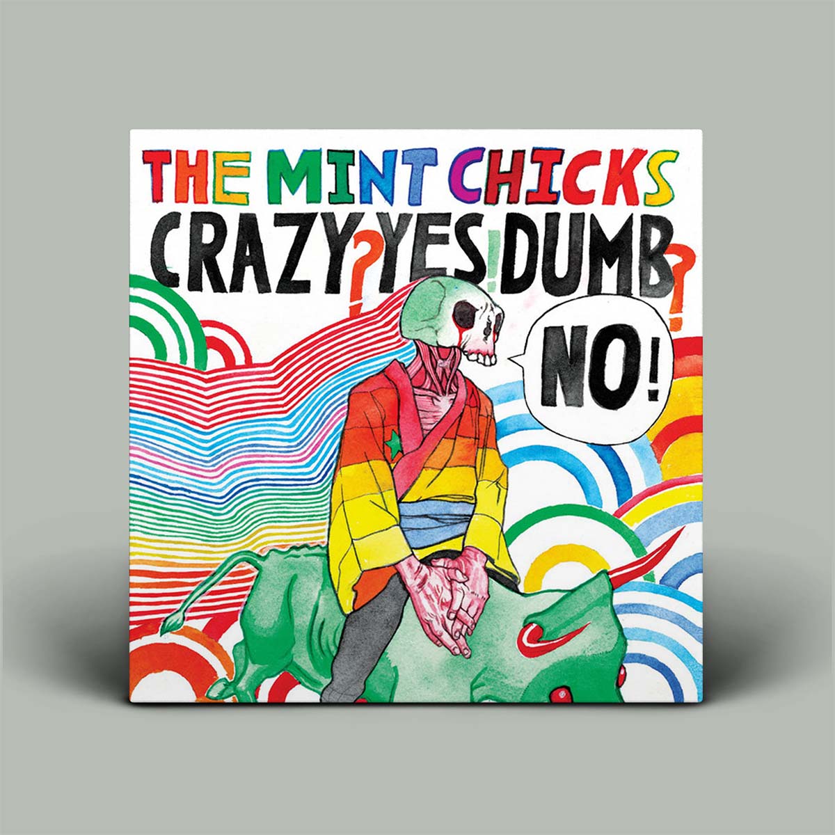 A square album cover for 'Crazy Yes Dumb' by The Mint Chicks, featuring a colorful illustration of a skeleton figure in a rainbow-striped jacket riding a green creature, with a speech bubble saying 'NO!', set against a light gray background.