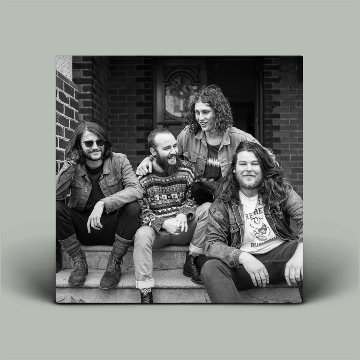 Black and white photo of four people sitting on steps in front of a brick building.