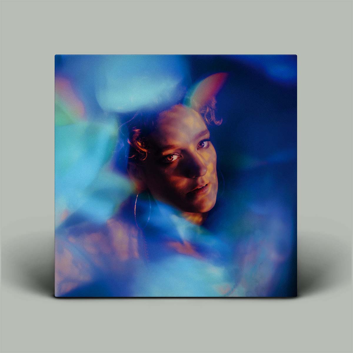Album cover with a person's face surrounded by colorful, abstract light effects on a gray background