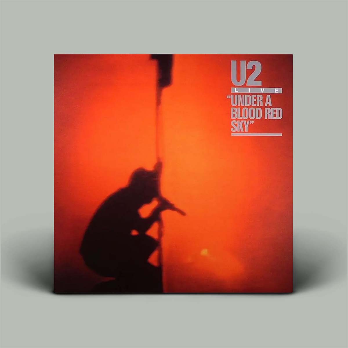 Album cover for U2's 'Under a Blood Red Sky' with a silhouette of a person and cat against an orange background.