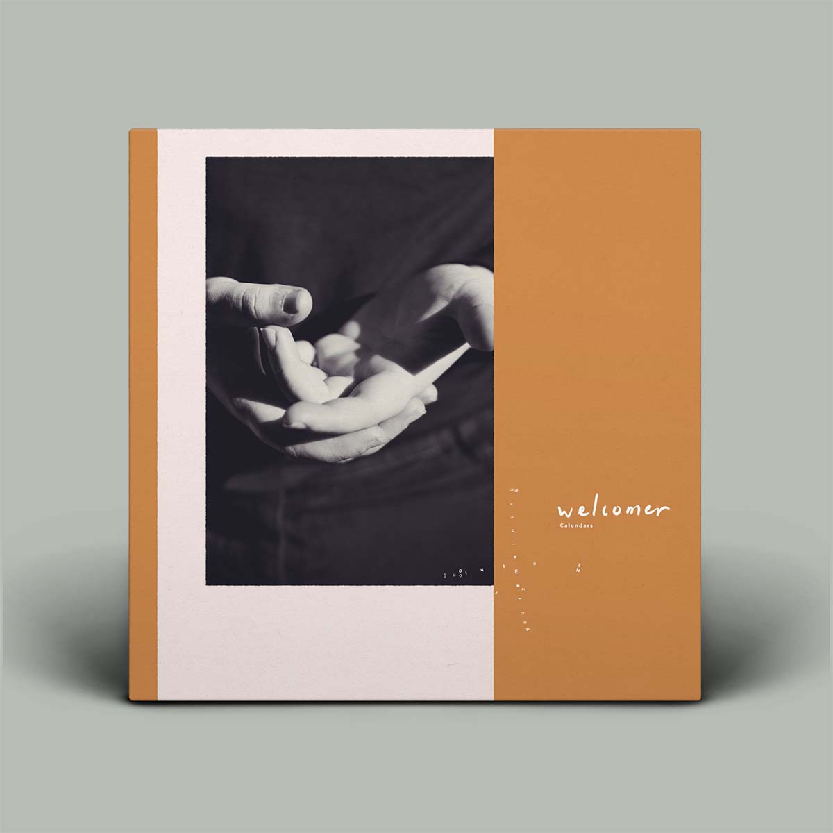 A square art print or book cover standing upright on a light gray background. The design is split vertically: the left half is off-white with a black-and-white photo of hands holding a small object, and the right half is a warm tan/orange field with the word 'welcomer' in white script and a few small white dots.
